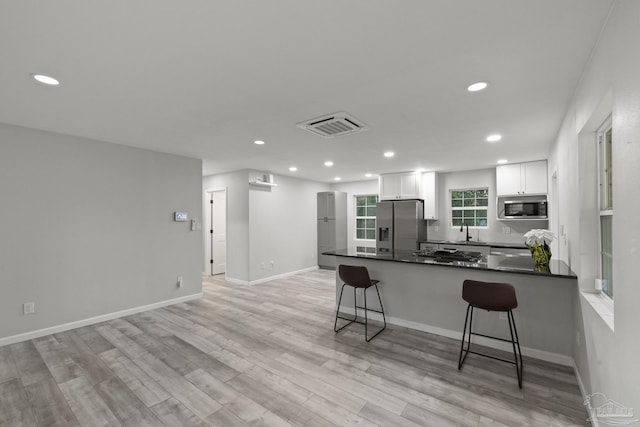 kitchen with kitchen peninsula, white cabinetry, stainless steel appliances, and light hardwood / wood-style flooring