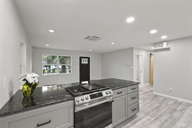 kitchen featuring dark stone counters, light hardwood / wood-style flooring, stainless steel gas range, gray cabinets, and a barn door