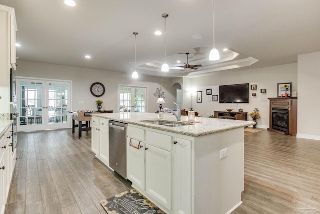 kitchen with stainless steel dishwasher, a tray ceiling, a sink, light wood-style flooring, and ceiling fan
