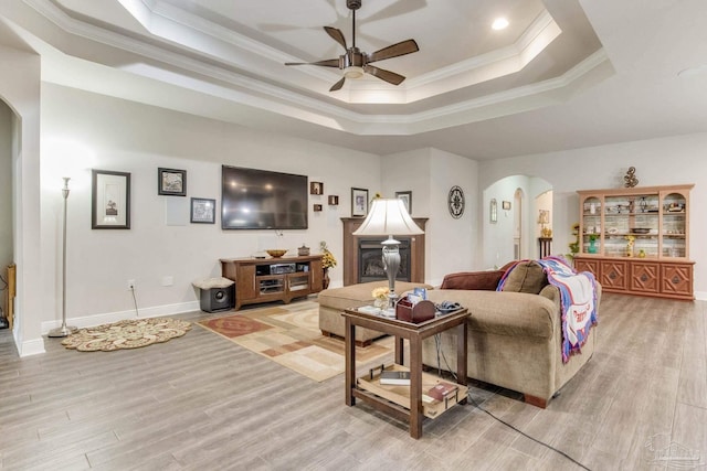 living room featuring light wood finished floors, a ceiling fan, arched walkways, and a raised ceiling