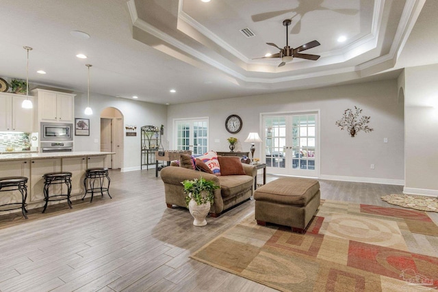 living area with crown molding, light wood-type flooring, ceiling fan, arched walkways, and visible vents