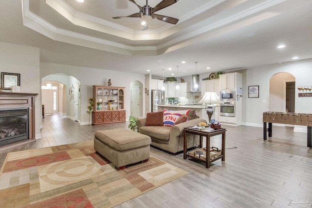 living area with baseboards, arched walkways, a ceiling fan, and a raised ceiling