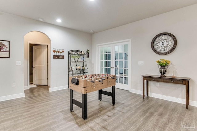 rec room with french doors, baseboards, arched walkways, and light wood-style flooring