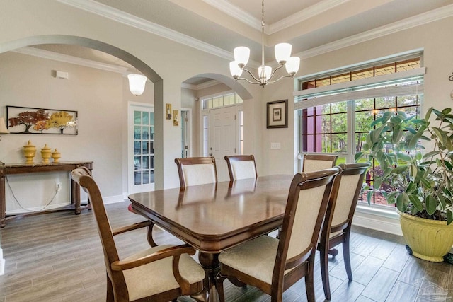 dining space with wood finished floors, arched walkways, crown molding, baseboards, and a chandelier