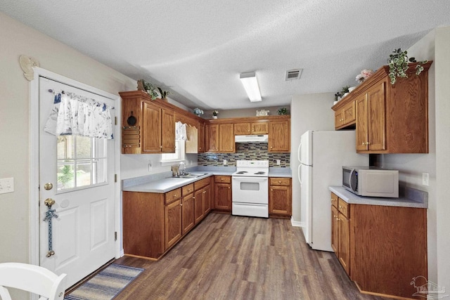 kitchen featuring sink, dark wood-type flooring, a textured ceiling, white appliances, and decorative backsplash