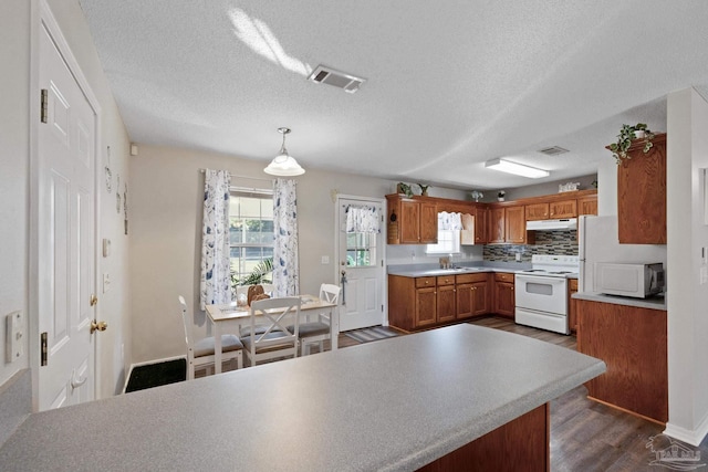 kitchen featuring dark wood-type flooring, hanging light fixtures, backsplash, a textured ceiling, and white appliances