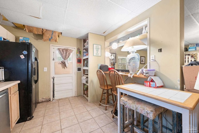 kitchen with kitchen peninsula, stainless steel dishwasher, tile counters, light tile patterned floors, and black refrigerator