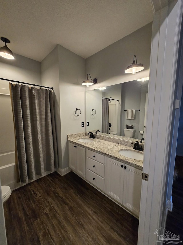 full bath with a sink, toilet, wood finished floors, and double vanity