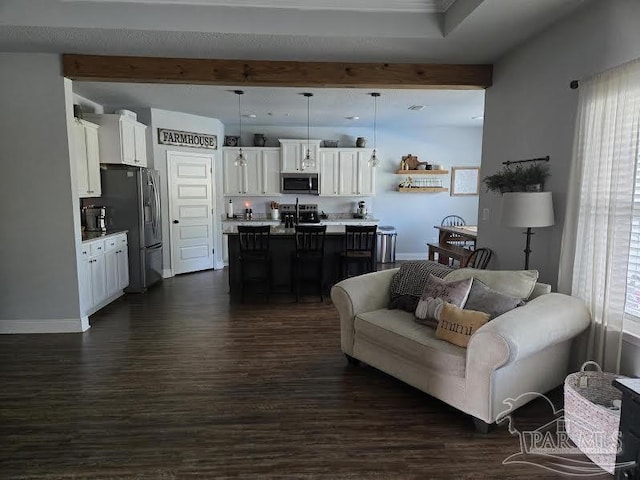 living room featuring dark wood finished floors, beam ceiling, and a healthy amount of sunlight