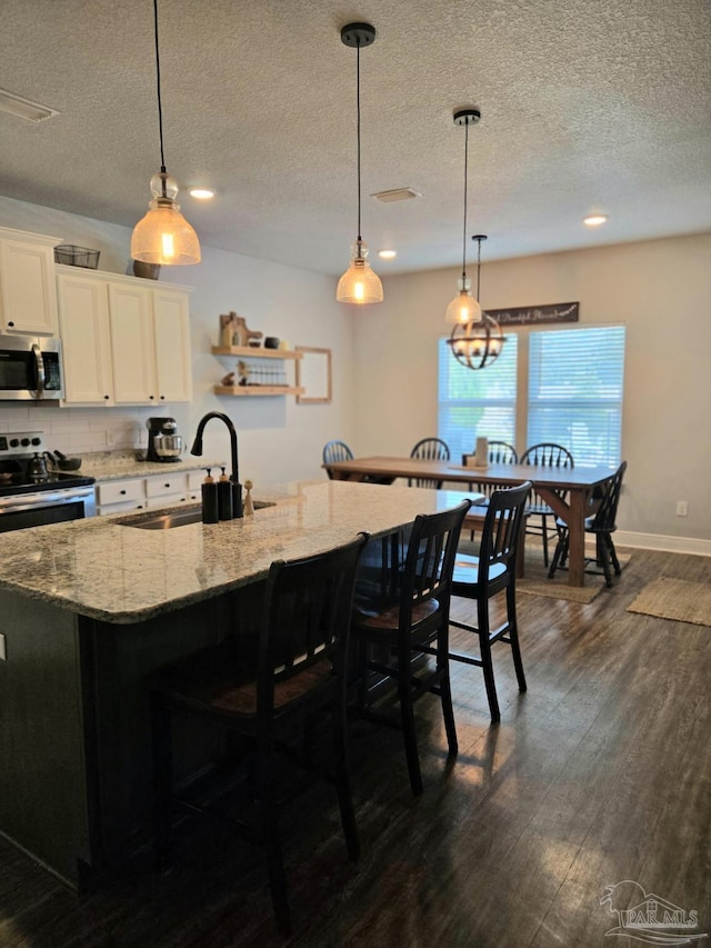 kitchen with a sink, light stone counters, dark wood-style floors, white cabinetry, and appliances with stainless steel finishes