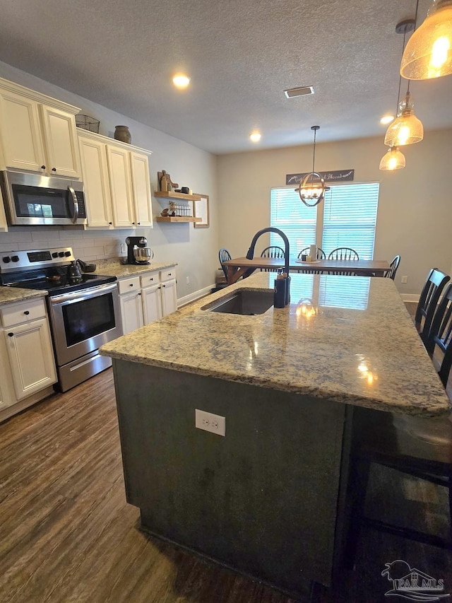 kitchen featuring light stone countertops, a center island with sink, dark wood finished floors, a sink, and stainless steel appliances