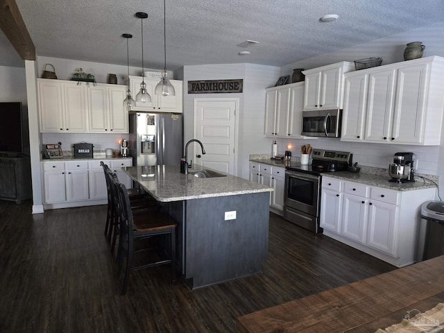 kitchen with an island with sink, dark wood-style flooring, a sink, stainless steel appliances, and white cabinets