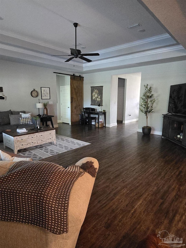 living room with a tray ceiling, wood finished floors, a barn door, crown molding, and baseboards