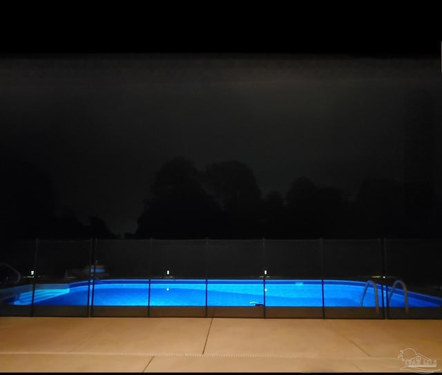 pool at night featuring a patio area, a fenced in pool, and fence