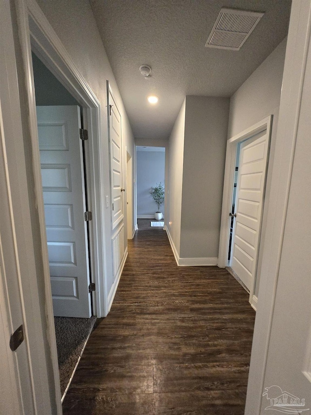 hall featuring visible vents, baseboards, a textured ceiling, and dark wood-style floors