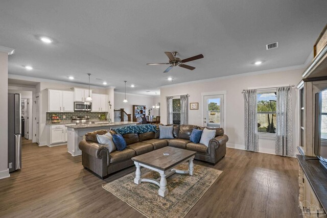 living room featuring ceiling fan, visible vents, wood finished floors, and ornamental molding