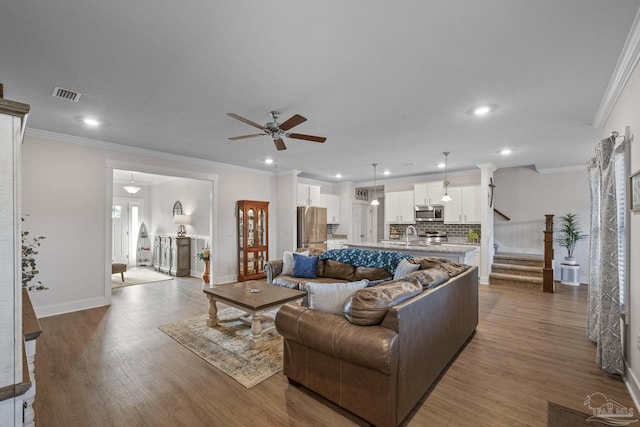 living room featuring dark wood-type flooring, visible vents, baseboards, ornamental molding, and stairway