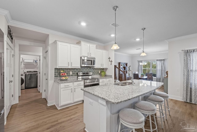 kitchen featuring washer / dryer, light wood-style flooring, a kitchen island with sink, stainless steel appliances, and a sink