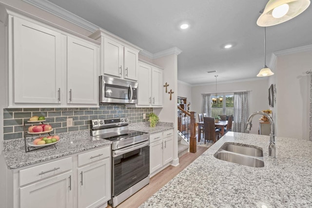 kitchen featuring appliances with stainless steel finishes, white cabinets, a sink, and ornamental molding