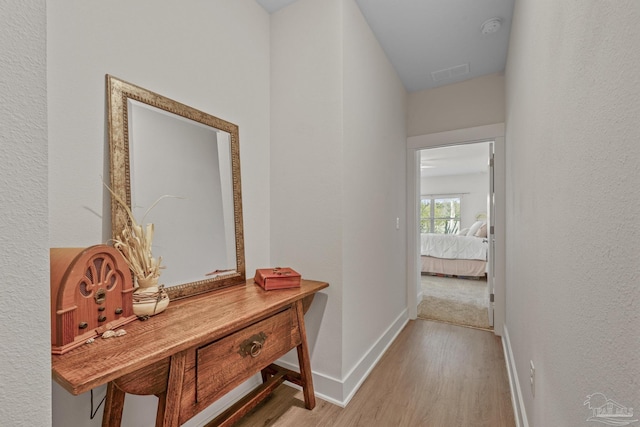 corridor featuring wood finished floors, visible vents, and baseboards