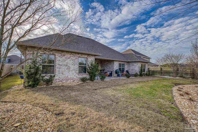 rear view of property featuring a shingled roof, a lawn, a fenced backyard, and brick siding