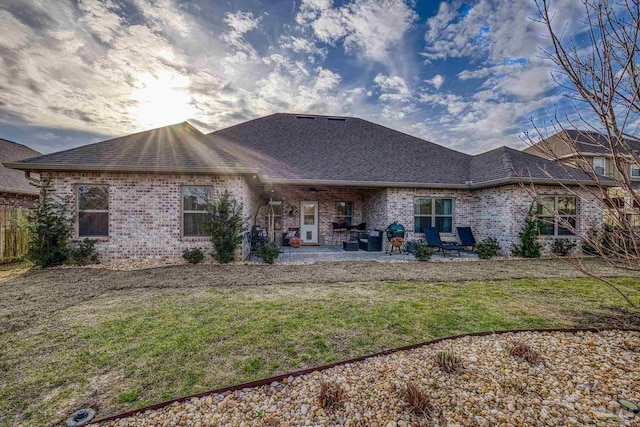 back of house with a yard, brick siding, roof with shingles, and a patio area