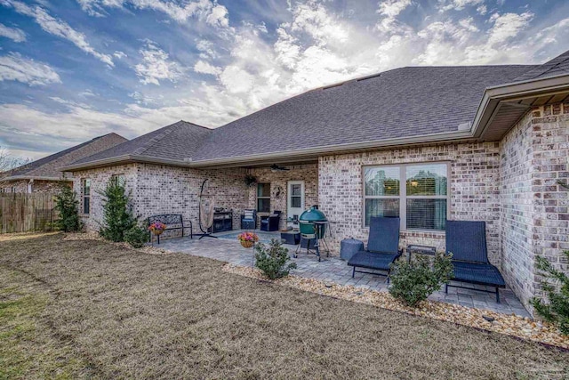 rear view of property featuring brick siding, a patio area, fence, and a shingled roof