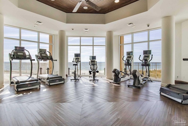 exercise room with a tray ceiling, hardwood / wood-style flooring, wood ceiling, ceiling fan, and floor to ceiling windows