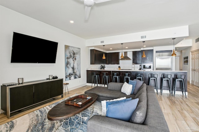 living room with ceiling fan, sink, and light wood-type flooring