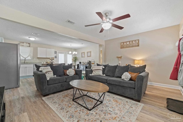 living room featuring ceiling fan with notable chandelier, light hardwood / wood-style floors, and a textured ceiling