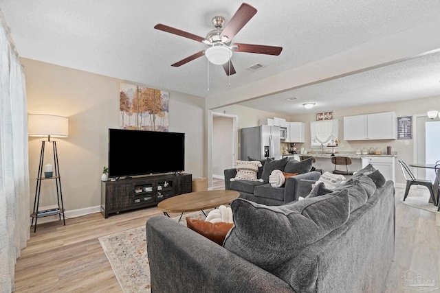 living room featuring ceiling fan, light hardwood / wood-style flooring, and a textured ceiling