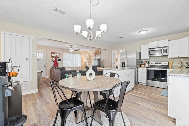 dining room with light wood-type flooring, ceiling fan with notable chandelier, and a textured ceiling