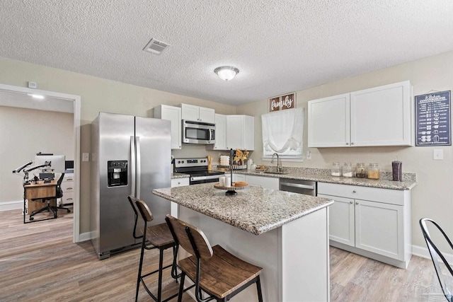 kitchen featuring light stone counters, stainless steel appliances, white cabinets, and a kitchen island