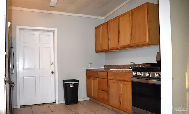 kitchen with light tile patterned flooring, crown molding, sink, and stainless steel range