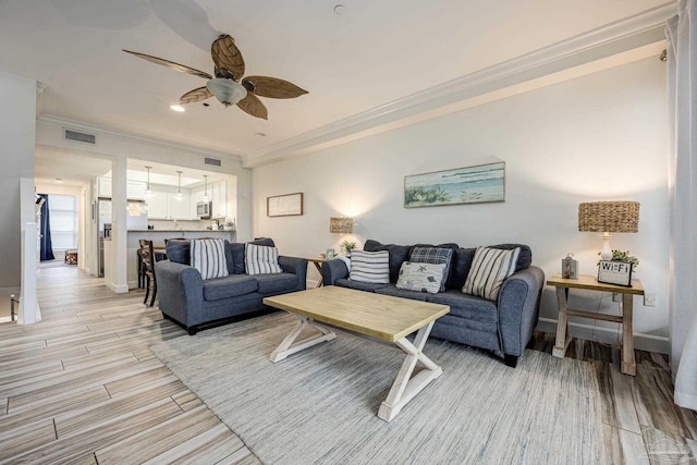 living room featuring ceiling fan, ornamental molding, and light wood-type flooring