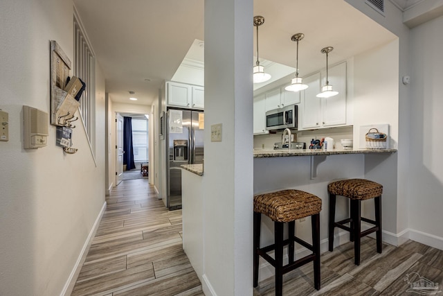 kitchen with light hardwood / wood-style floors, light stone countertops, white cabinetry, and stainless steel appliances