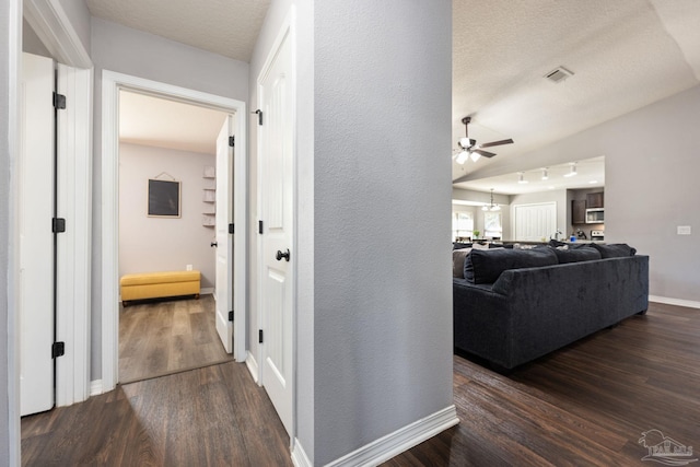 hall with a textured ceiling, dark wood-type flooring, and vaulted ceiling