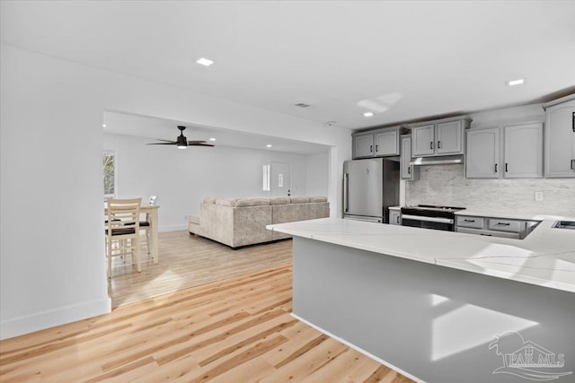 kitchen with appliances with stainless steel finishes, kitchen peninsula, gray cabinets, light hardwood / wood-style floors, and decorative backsplash