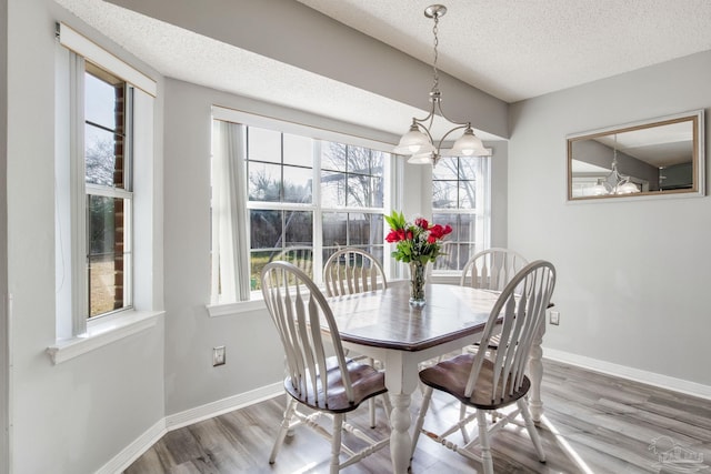 dining space featuring a chandelier, a textured ceiling, baseboards, and wood finished floors