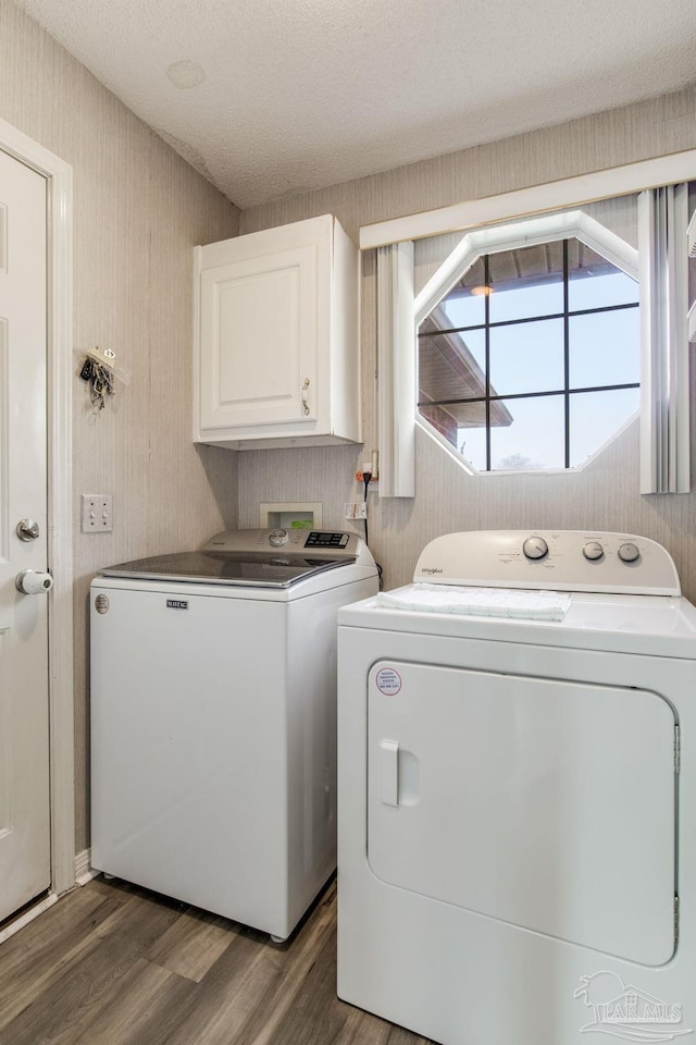 clothes washing area with cabinet space, a textured ceiling, separate washer and dryer, wood finished floors, and wallpapered walls