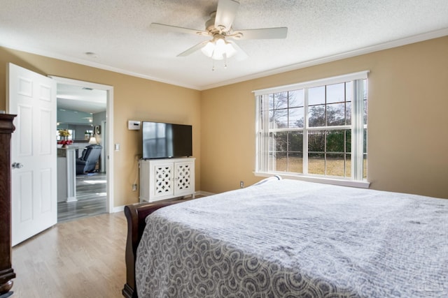 bedroom with a textured ceiling, wood finished floors, a ceiling fan, baseboards, and crown molding