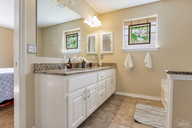 ensuite bathroom featuring double vanity, ensuite bath, baseboards, and a textured ceiling