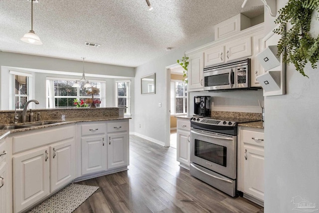 kitchen featuring white cabinets, dark wood-type flooring, stainless steel appliances, pendant lighting, and a sink