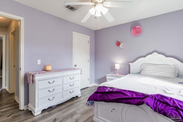 bedroom featuring visible vents, ceiling fan, a textured ceiling, wood finished floors, and baseboards