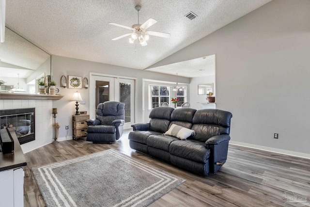 living area with a textured ceiling, a tile fireplace, wood finished floors, visible vents, and vaulted ceiling