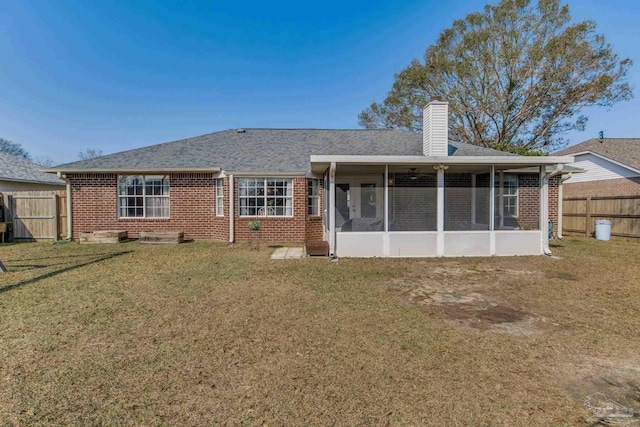 back of house featuring brick siding, fence, a sunroom, a yard, and a chimney