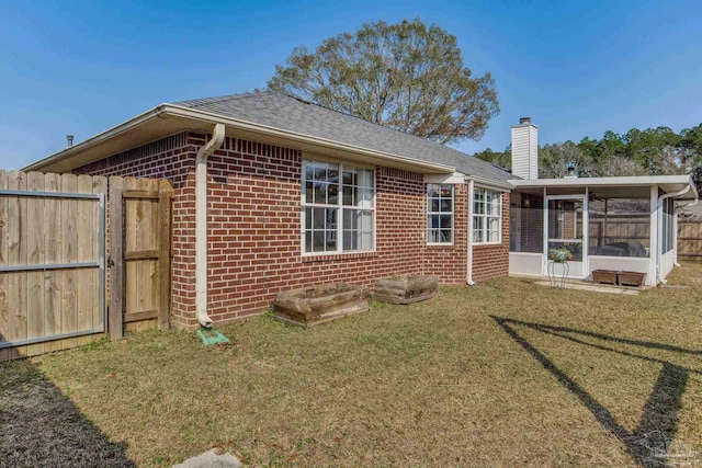 rear view of house featuring brick siding, a chimney, a lawn, a sunroom, and fence