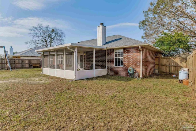 rear view of property with brick siding, a chimney, a lawn, a sunroom, and a fenced backyard