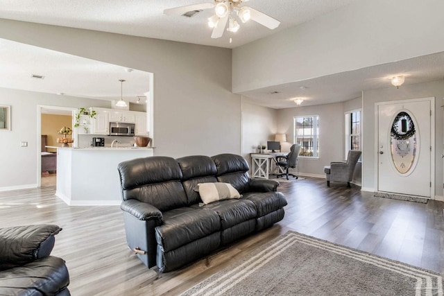 living room featuring vaulted ceiling, light wood finished floors, visible vents, and baseboards