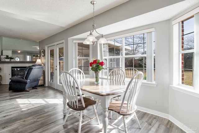 dining area featuring french doors, a glass covered fireplace, a textured ceiling, wood finished floors, and baseboards